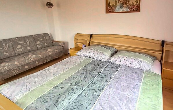 Una camera da letto con un letto, una testiera in legno, un divano grigio con motivo decorativo e un piccolo comodino.