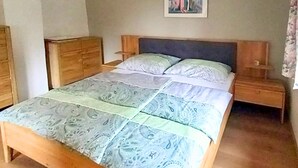 Ein Schlafzimmer mit einem hölzernen Bett, einem Nachttisch, einer Kommode und einem Bild an der Wand.