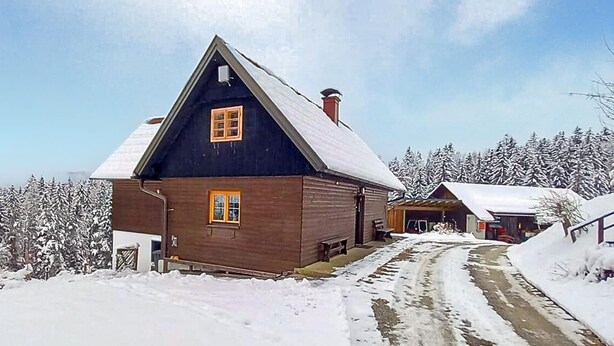 Eine Holzhütte mit einem steilen Satteldach, einer Veranda und einer verschneiten Landschaft.
