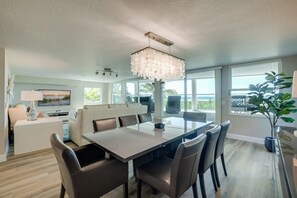 A modern dining area with a large table and chairs, a chandelier, and a view of the outdoors.