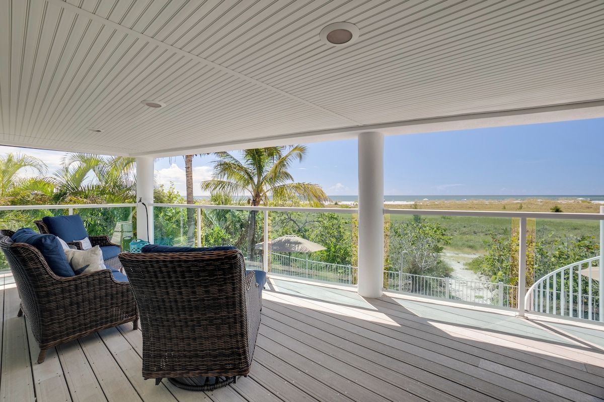 A covered outdoor area with wicker furniture and a view of the beach.