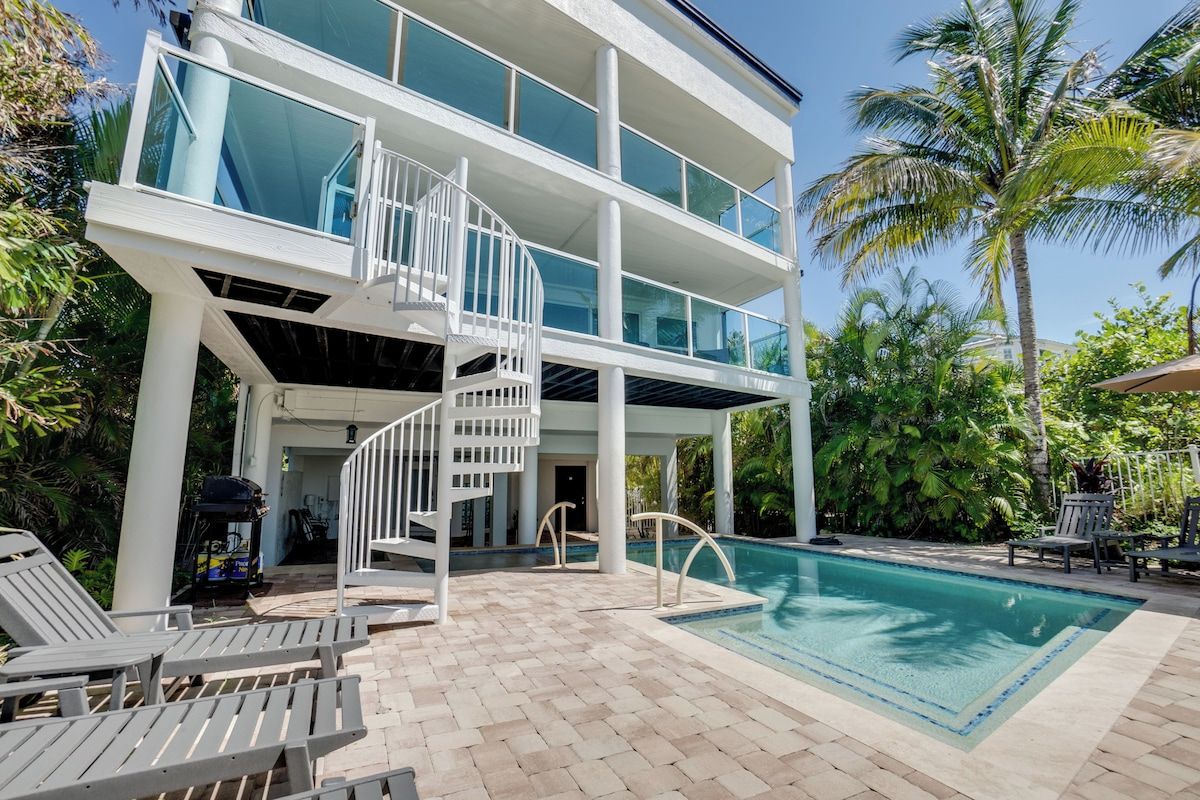 A modern two-story building with a pool, outdoor seating, and a spiral staircase.