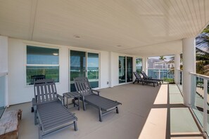 Een overdekt terras met lounge fauteuils en een glazen balustrade.