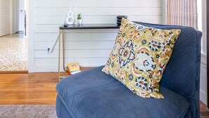 A living room with a blue sofa, a TV mounted on the wall, a small table with decorative items, and a patterned pillow. - Vintage Rosedale Bungalow in Rosedale (Austin)
