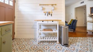 A kitchen with a wooden countertop, white cabinets, a stainless steel trash can, and a hanging pot rack. - Vintage Rosedale Bungalow in Rosedale (Austin)