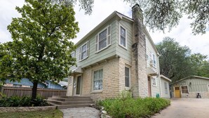 A two-story house with a stone facade, a front porch, and a small attached garage. - Vintage Rosedale Bungalow in Rosedale (Austin)