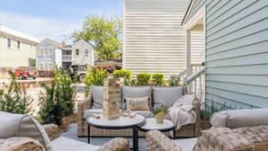 Un espace patio aménagé avec des meubles en osier, une tour de jeu de Jenga et un coin salon confortable.