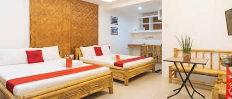 A hotel room with two beds, a small table, and a bench.