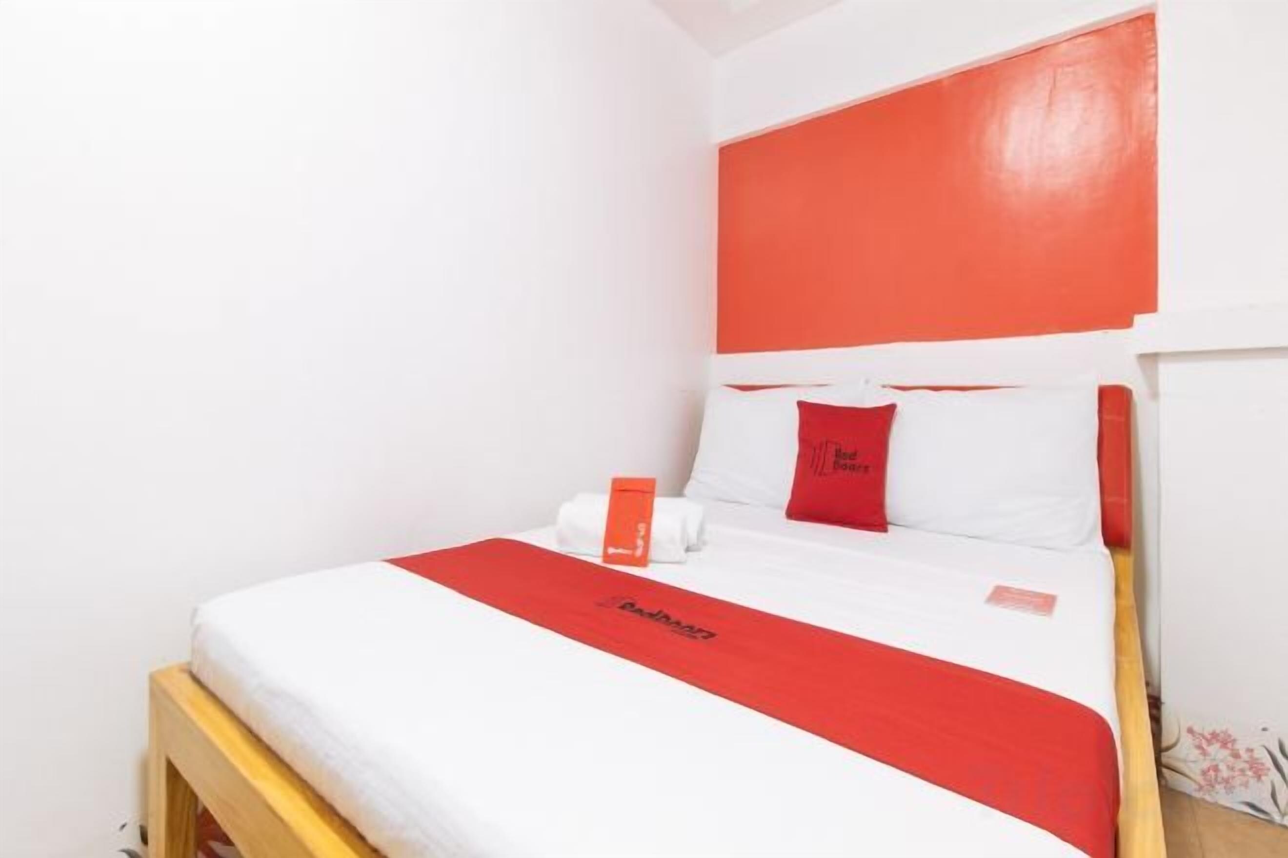 Een hotelkamer met een bed, een kleurenschema in rood en wit, en een houten hoofdbord.