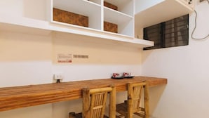 A kitchen area with a wooden countertop, two bamboo chairs, a white shelf with storage boxes, and a window with a blind. - RedDoorz @ DBuilders Rooms Ph1 Taguig (Taguig)