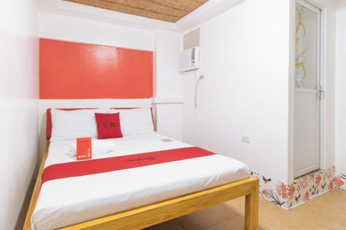 A hotel room with a bed, a wooden headboard, a red accent wall, and a door with a floral design.
