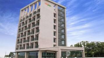 A multi-story building with a modern architectural design, featuring a central entrance with a glass facade and a series of balconies on each floor.