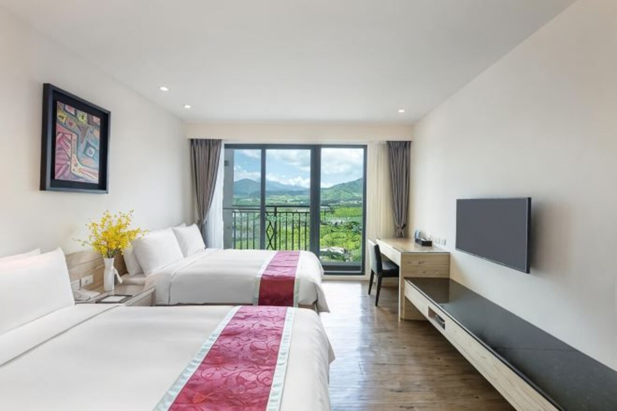 Une chambre d’hôtel avec deux lits, un bureau, une télévision et un balcon avec vue.