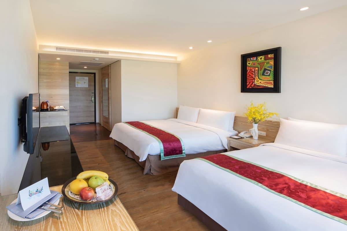 Ein Hotelzimmer mit zwei Betten, einem Fernseher, einem Schreibtisch und einer Obstschale.
