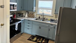 Una cocina con armarios azul claro, un refrigerador de acero inoxidable, un microondas, un lavamanos y un ventanal con persianas.