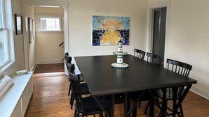Un comedor con una mesa de madera oscura, sillas negras, un banco blanco y un cuadro de un faro.