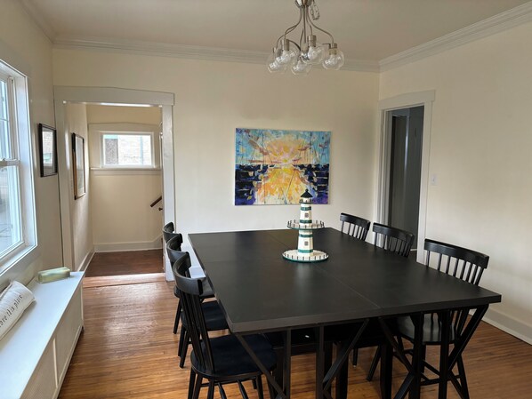 A dining room with a dark wooden table, black chairs, a white bench, and a painting of a lighthouse.