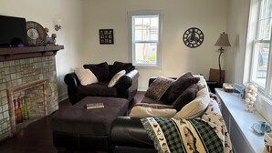 Una sala de estar con chimenea, dos sofás, un reloj y un ventanal con vistas.