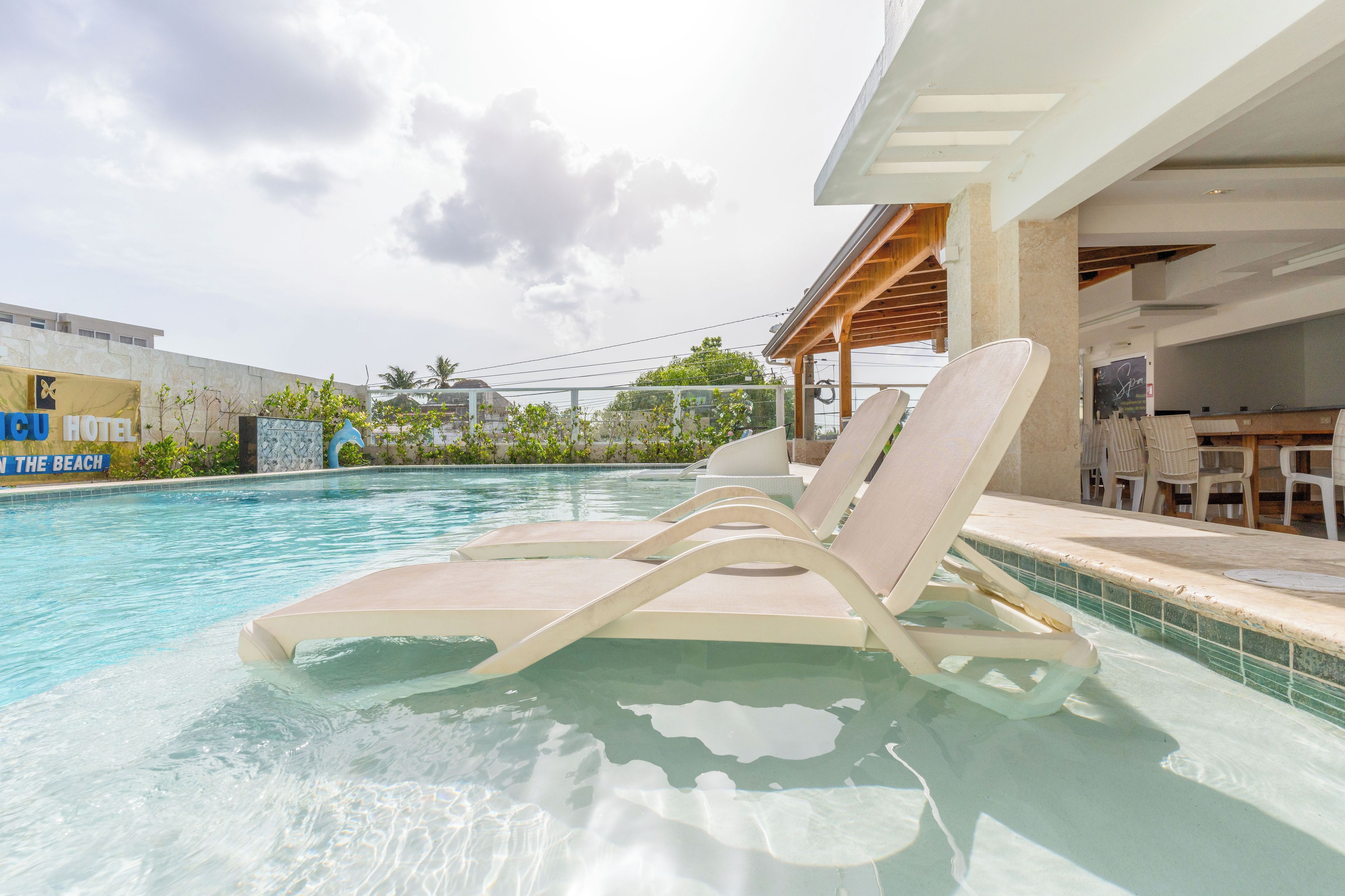 A swimming pool with lounge chairs, a covered patio area, and a sign for 'Hotel in the Beach'.