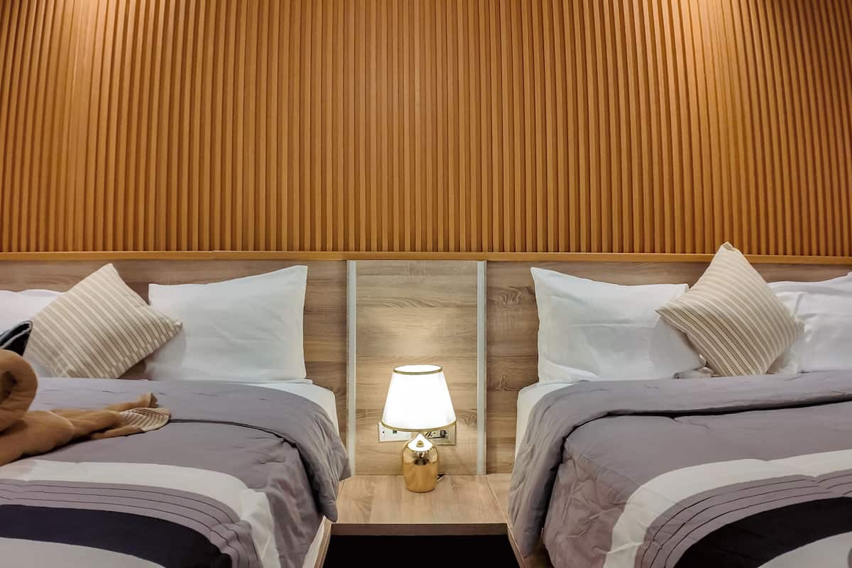 A hotel room with two beds, a nightstand with a lamp, and a wooden headboard.