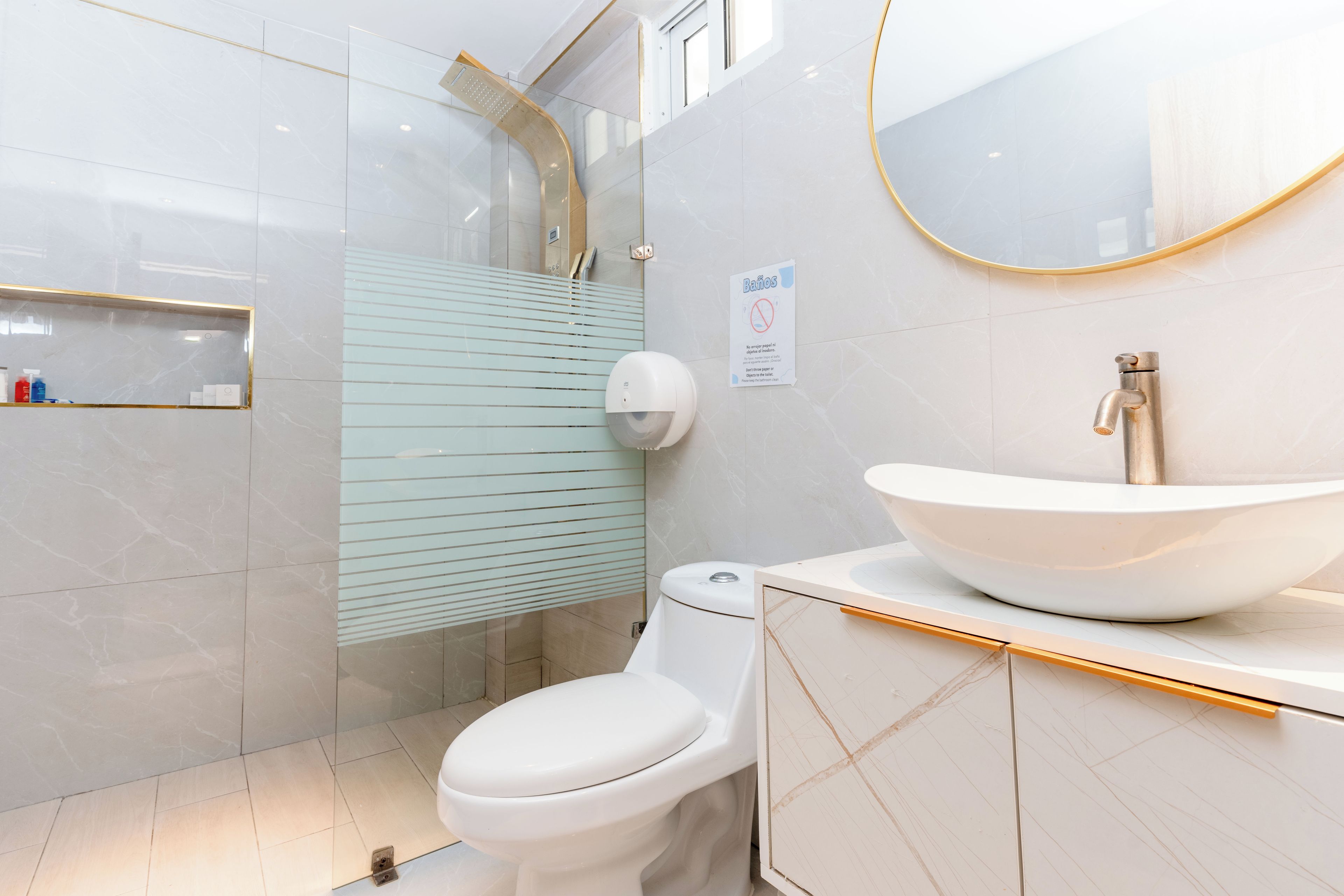 A modern bathroom with a white toilet, a large vessel sink, and a glass shower enclosure.