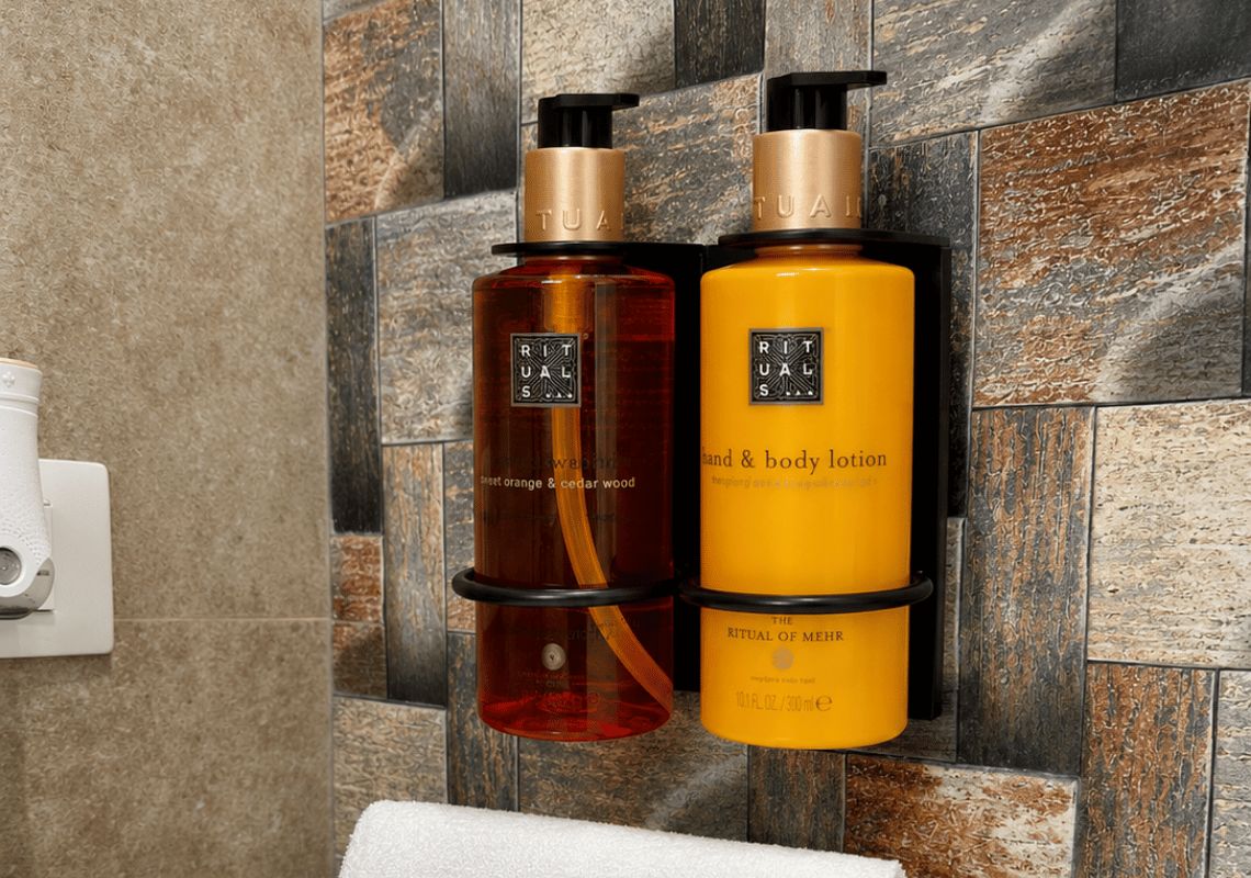Dos botellas de crema para manos y cuerpo sobre una pared de azulejos.