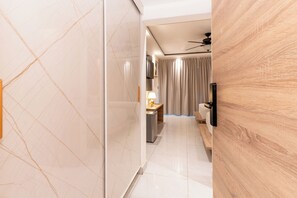 A hotel corridor with a marble wall, a wooden door, a ceiling fan, a bed, and a bathroom with a mirror and sink. - Casual On the Beach Bayahibe by Casual Hoteles (Bayahíbe)