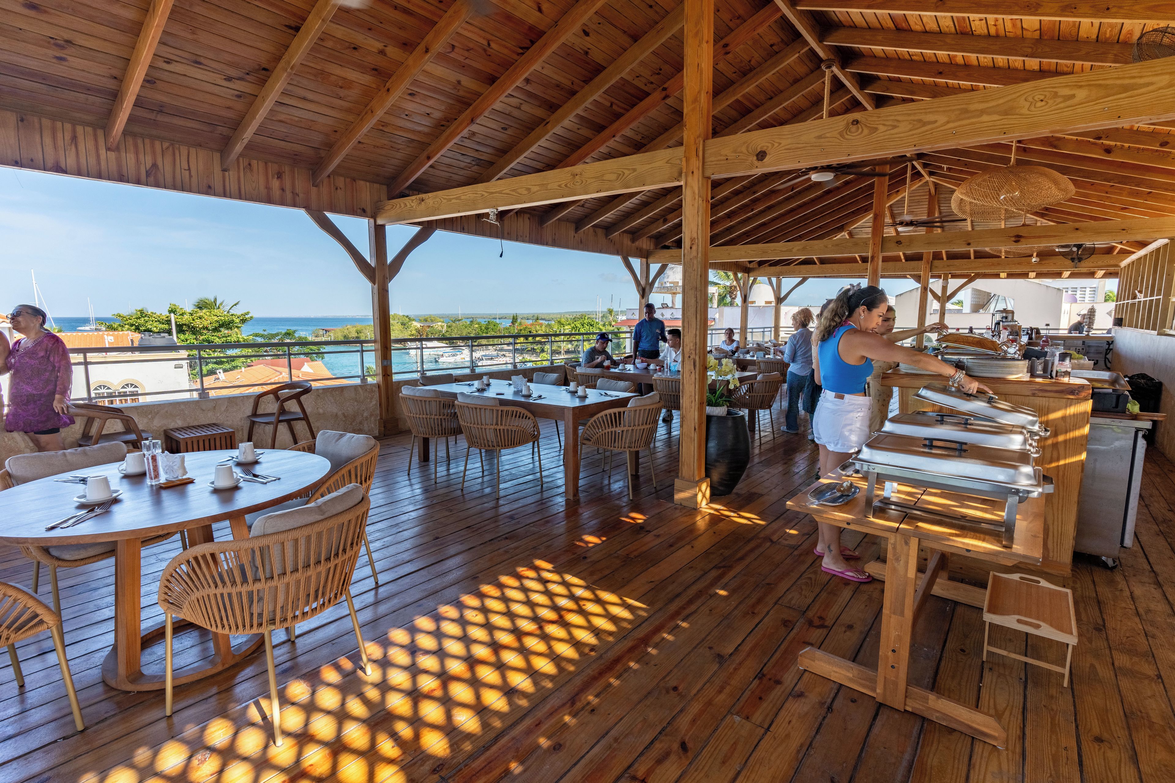 Ein Essbereich im Freien mit Holztischen und -stühlen, einer Grillstation und Blick aufs Meer.
