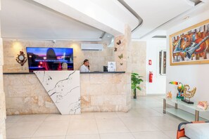A reception area with a marble counter, a television displaying a music video, and a receptionist. - Casual On the Beach Bayahibe by Casual Hoteles (Bayahíbe)