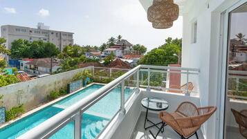 A balcony with a glass railing overlooking a swimming pool and a cityscape.
