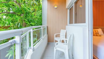 A balcony with a white railing, a seating area with two white chairs, and a bed with a white headboard and pillows.