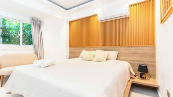 Quarto moderno com uma cama grande, mesa de cabeceira com abajur e ar condicionado na parede.