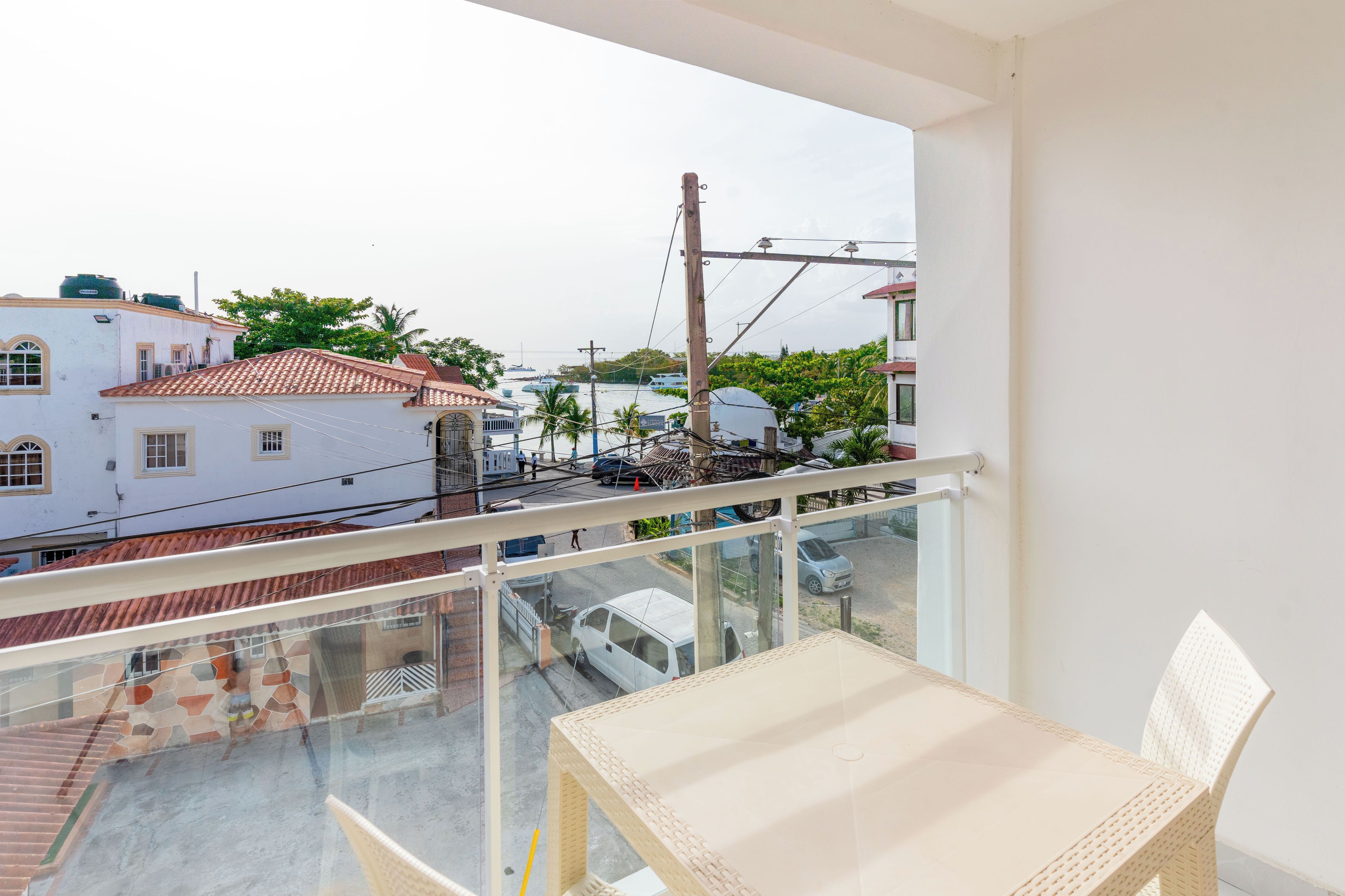 A balcony with a view of a street, a white building, and a parked car.