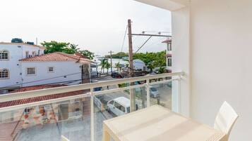 A balcony with a view of a street, a white building, and a parked car.