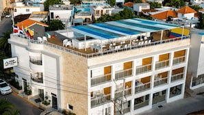 Un hotel de varios pisos con piscina en la azotea, balcones y un letrero que indica un restaurante informal dentro del establecimiento.