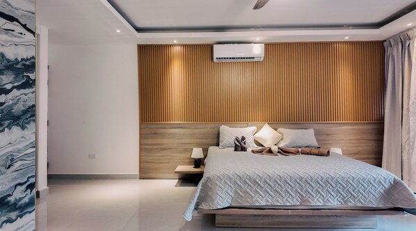A modern bedroom with a wooden headboard, a bed with a quilted cover, and a nightstand with a lamp. - Casual On the Beach Bayahibe by Casual Hoteles (Bayahíbe)
