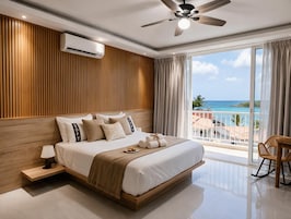 A modern bedroom with a large bed, a ceiling fan, an air conditioning unit, and a balcony with a view of the ocean.