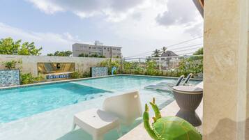A swimming pool with clear blue water, surrounded by a stone wall and greenery. There are lounge chairs and a decorative sculpture near the pool.