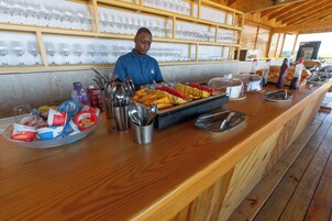 Mostrador de buffet con diversas opciones de comida, utensilios y una persona sirviendo.