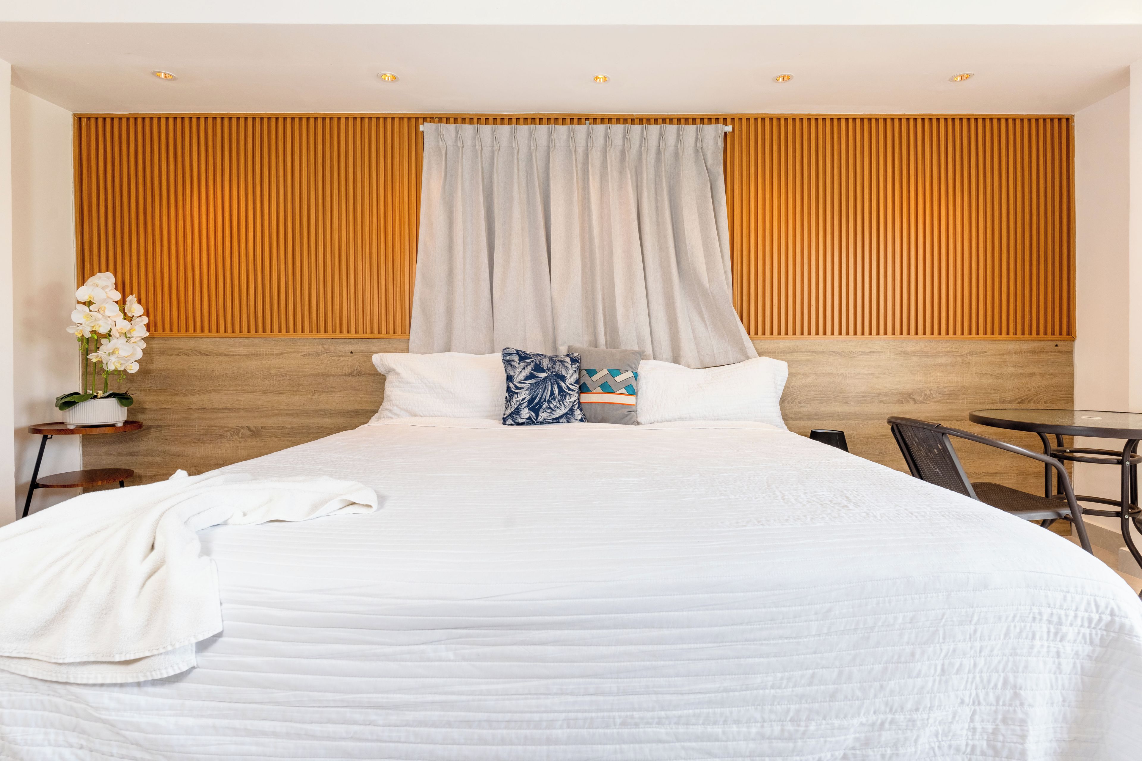 Une chambre d’hôtel moderne avec un grand lit, une tête de lit en bois, une table à manger et une plante en pot.