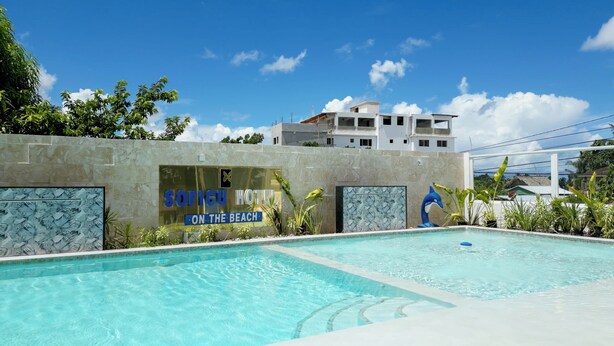 A hotel sign with a pool area, including a dolphin sculpture and tropical plants. - Soficu Hotel On The Beach (Bayahíbe)