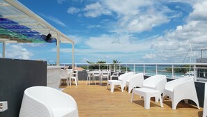 A deck with white wicker furniture, a covered area with a glass ceiling, and a view of the sea. - Soficu Hotel On The Beach (Bayahíbe)