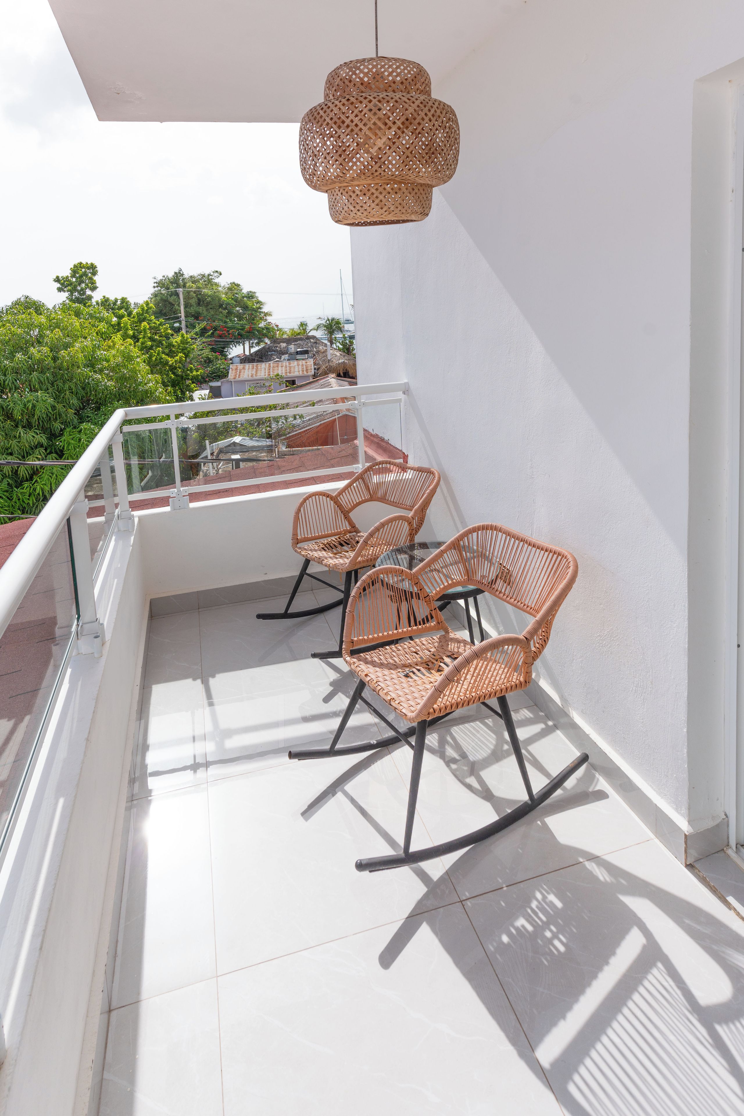 Ein Balkon mit zwei Korbstühlen, einer hängenden Korb-Leuchte und Blick auf Grünflächen und Gebäude im Hintergrund.