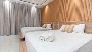 Une chambre d’hôtel avec deux lits, une tête de lit en bois, des rideaux gris et un sol carrelé.