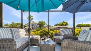 An outdoor seating area with wicker furniture, a glass table, and umbrellas.