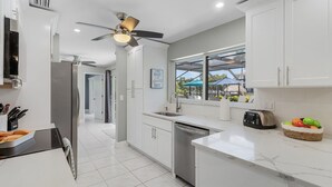 A modern kitchen with white cabinetry, a built-in dishwasher, a toaster, and a window overlooking a pool area.
