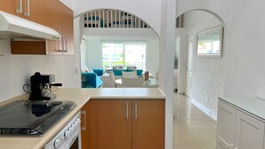 A kitchen with wooden cabinets, a stove, and a dining area with a blue couch and white chairs. - Zafiro 316 Acapulco Diamante (Acapulco de Juárez)