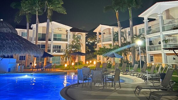 A swimming pool area with lounge chairs and umbrellas, surrounded by palm trees and hotel buildings. - Zafiro 316 Acapulco Diamante (Acapulco de Juárez)