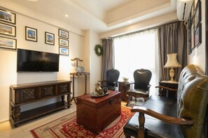 Sala de estar com televisão, armário de madeira, sofá de couro e tapete estampado.