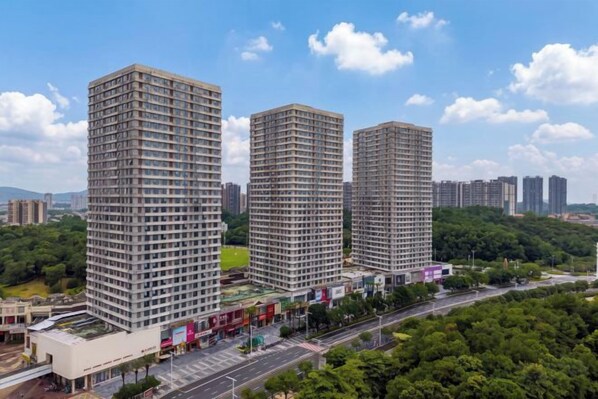 Un edificio alto con varios pisos, rodeado de vegetación y otros edificios.